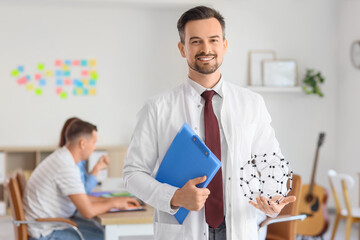 Fototapeta premium Male Science teacher with clipboard and molecular model in school office