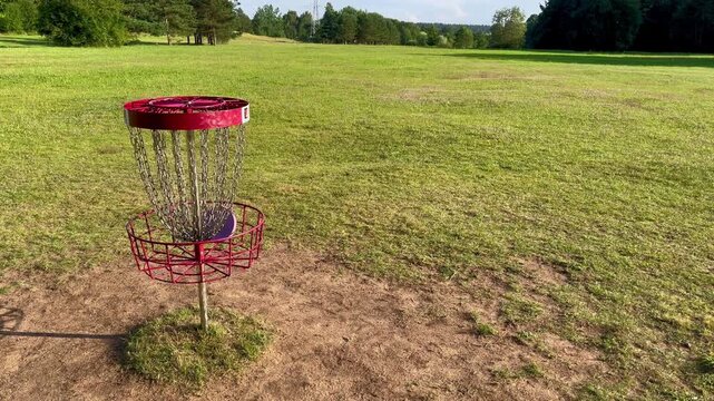 Disc golf basket with red chains in sunny open field in Tukums countryside, Latvia