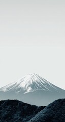 Snowy mountain peak rising above dark foothills against a pale sky