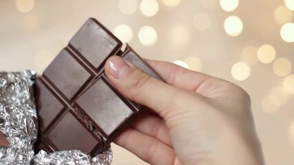 Close-up of a woman's hands gently unwrapping a dark chocolate bar.