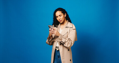 Phone, confused and reading with woman in studio for phishing, fake profile and social media scam. Clickbait link, password check and mockup space with person on blue background for security update