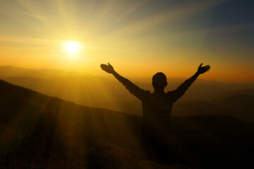 Silhouette of a man with raised hands on the top of the mountain.