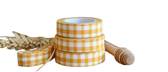 Stacked rolls of yellow and white checkered tape with a wooden honey dipper and wheat