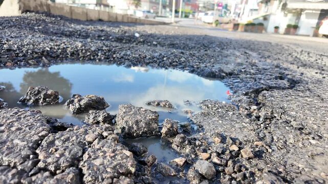 A large pothole on a city street collects rainwater under sunlight