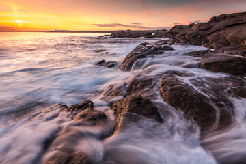Lorient Morbihan Ocean surf rushing over dark granite rocks under a colorful sunset sky.