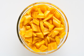 An overhead, closeup shot of a glass bowl filled with fresh, bright yellow jackfruit chunks.