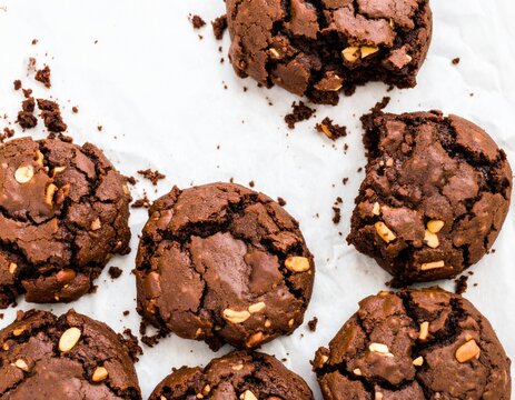 Overhead flat lay of chewy brookie featuring cracked cookie surface and gooey chocolate brownie interior, with broken piece and scattered crumbs on rustic parchment paper background
