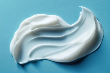 Fototapeta premium Smooth white cream spread artistically on a blue textured surface creating soft flowing patterns