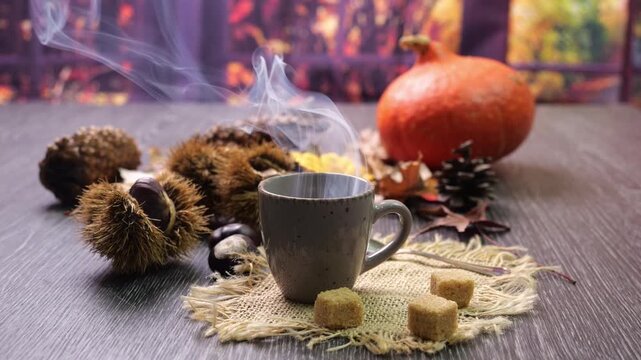 Tazzina di caff&egrave; bollente fumante sul tavolo con cubetti di zucchero, ricci e castagne, foglie secche e zucca