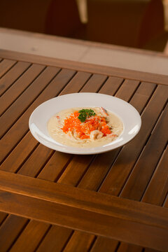 Creamy Shrimp Pasta with Tobiko Roe. Elegant plate of Italian spaghetti in a rich, light sauce, topped with succulent shrimp and vibrant orange tobiko roe. Gourmet seafood pasta on a wooden table.