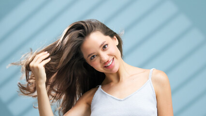 Fototapeta premium Young woman with healthy skin and flowing hair, smiling while playfully tossing her hair in a bright, airy space, showcasing a vibrant atmosphere and emphasizing the beauty of skincare and self-care