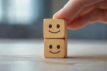 Hand stacking two wooden cubes with smiling faces on a smooth surface conveying happiness and positivity in soft natural light