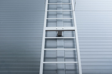 Industrial vertical safety ladder with protective cage mounted on modern metal wall, minimalistic architectural design element, symbolizing access, safety, construction, and industrial engineering