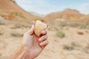 Hand holding a translucent stone while colorful mountains of Aktau rise majestically in the background, creating a stunning desert landscape