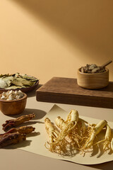Minimalist vertical frame of ginseng root placed beside wooden trays and dried herbs, styled against a clean beige background for clarity.