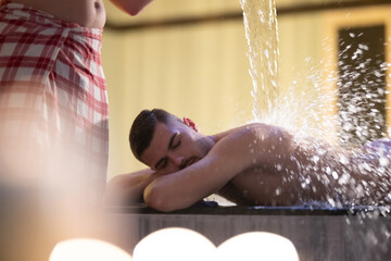 Man receiving water therapy inside a traditional Turkish hammam with ornate details.