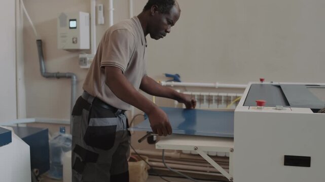 African American print shop worker printing poster on blue paper using modern equipment