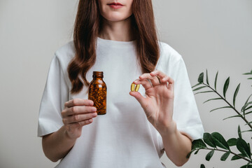 A woman holds omega-3 fish oil capsules. Healthy lifestyle, prevention and treatment of diseases. The woman takes and drinks dietary supplements and vitamins for skin, nails and hair. 