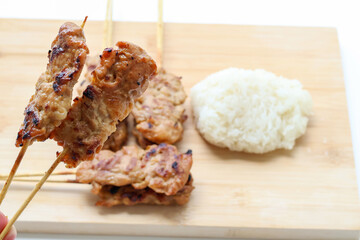 Hand holding two grilled pork skewers, Thai street food often enjoyed for breakfast. with copy space