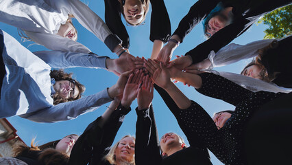 Students uniting in a circle with hands clasped, showcasing teamwork and togetherness on a sunny school day