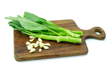 Chinese broccoli and garlic cloves on a wooden cutting board isolated on white background close up stack clipping path, preparation for stir fry in kitchen