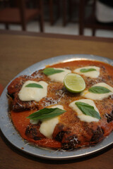 Delicious chicken parmesan with tomato sauce, mozzarella, basil, and lime garnish.