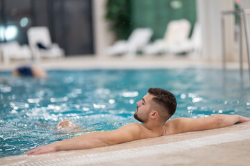 Man floating peacefully in warm spa water with eyes closed and arms outstretched on the edge of the pool.