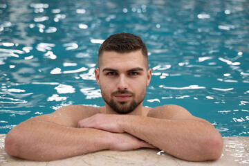 Man resting on the edge of a large indoor pool with a calm expression and relaxed posture.