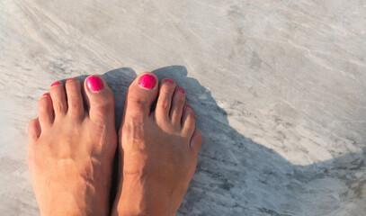 Top view of feet with red nails standing on marble floor capturing a serene summer moment.