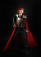 Obraz premium Fantasy warrior woman model in historical medieval armour costume, red fairytale cloak, cinematic portrait of strong fantasy knight holding sword. Epic standing pose, dark studio background