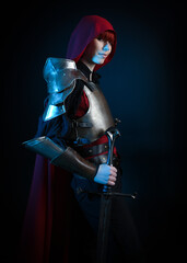 Naklejka premium Fantasy warrior woman with red hair in historical medieval armour costume and red fairytale cloak, cinematic studio portrait of strong heroine knight, epic battle pose, dramatic silhouette figure.