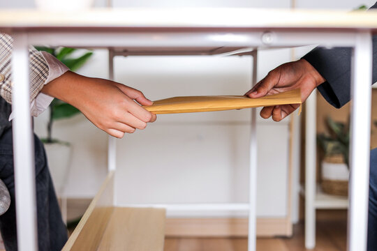 Two Hands Passing Yellow Envelope to Each Other Under Light Wooden Table, Bribery Concept