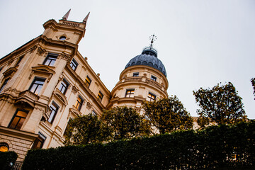 Looking up at a classic European building with a rounded dome and ornate facade against a grey,...