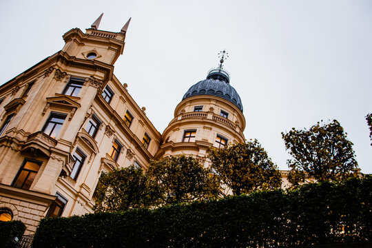 Looking up at a classic European building with a rounded dome and ornate facade against a grey, overcast sky.
