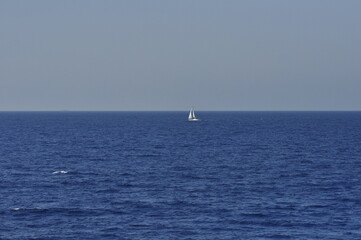A sailboat gracefully gliding across the horizon in a calm and tranquil blue ocean