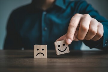 A person holding a smiling face block over a sad face block on a wooden surface indoors