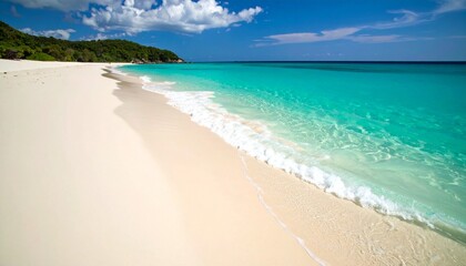 Fototapeta premium Pristine white sand beach meets turquoise ocean water with gentle waves, backed by lush green hills under a blue sky.