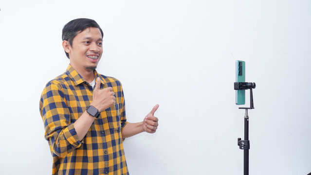 Asian young man recording video content, dancing on smartphone camera at studio. Positive millennial filming for social media, using mobile device.