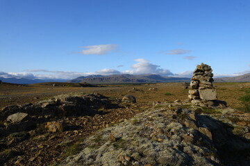 Wide open volcanic plain with rocky ground, distant mountains and a dramatic sky filled with white clouds in evening light