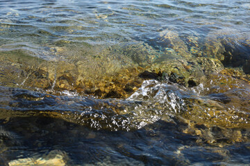 Clear sea wave flowing over rocky seabed in sunlight