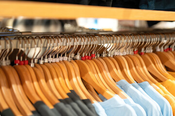 Colorful bright cotton T-Shirt with wooden hanger were hanging on the rack, for sale at modern apparel fashion store. Close-up with selective focus.