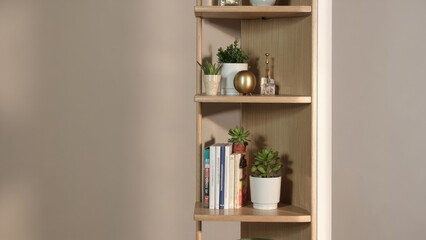 Wooden corner shelf unit with plants books and decorative objects against a neutral wall in a well lit room