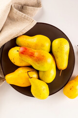 ripe yellow-green pears on plate on a white table.