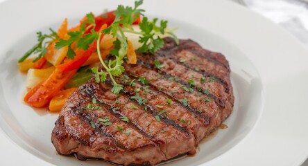 Grilled steak served with vegetables and garnish on a white plate, closeup shot.