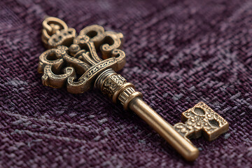 Golden key with ornate crown top on purple fabric.