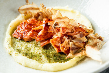 Gourmet dish with mashed potatoes, glazed meat slices, bonito flakes, and herbs, artfully plated on a white ceramic plate for elegant food presentation