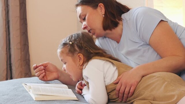 Mother supports her daughters early reading skills while sharing a bedtime story. Preschool literacy and home education. Close up.