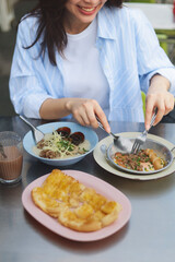 Smiling Asian woman eating Thai breakfast at local street food market, authentic lifestyle and happiness concept.