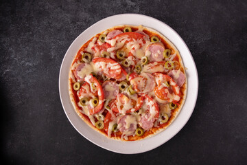 Round pizza on a plate, on a black background, space for text, top view