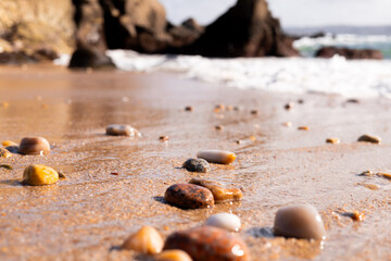 Pebble strewn beach with gentle waves and rocky background